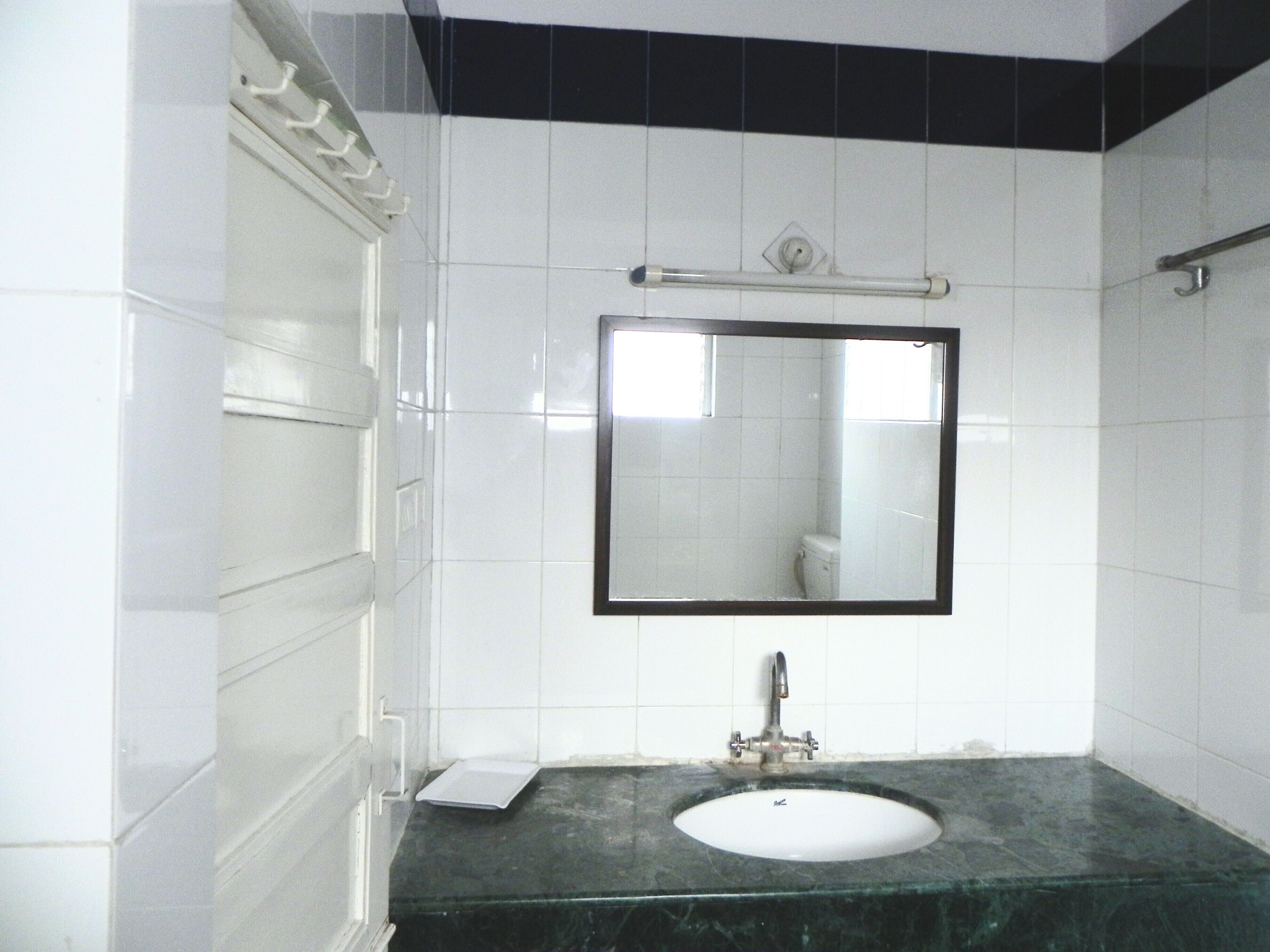 A bathroom with white tiled walls, a black-framed mirror, a sink with a faucet, and a towel rack.