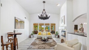A spacious living room with a chandelier, a sofa, a coffee table, and a dining area with chairs and a table. - Palm View Ranch - 1 acre mini resort! (Palm Desert)