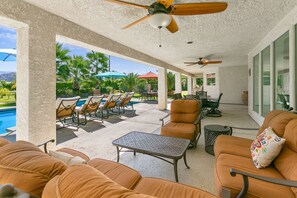 Un espacio al aire libre techado con sillones de descanso, una piscina y ventiladores de techo.