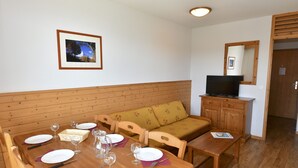 Zona pranzo con tavolo in legno apparecchiato, divano e televisione su mobile in legno.