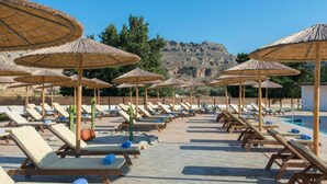 A poolside area with sun loungers and thatched umbrellas, a pool, and a mountainous backdrop. - Anavadia Hotel By Anayia All Inclusive Resorts (Rhodes)