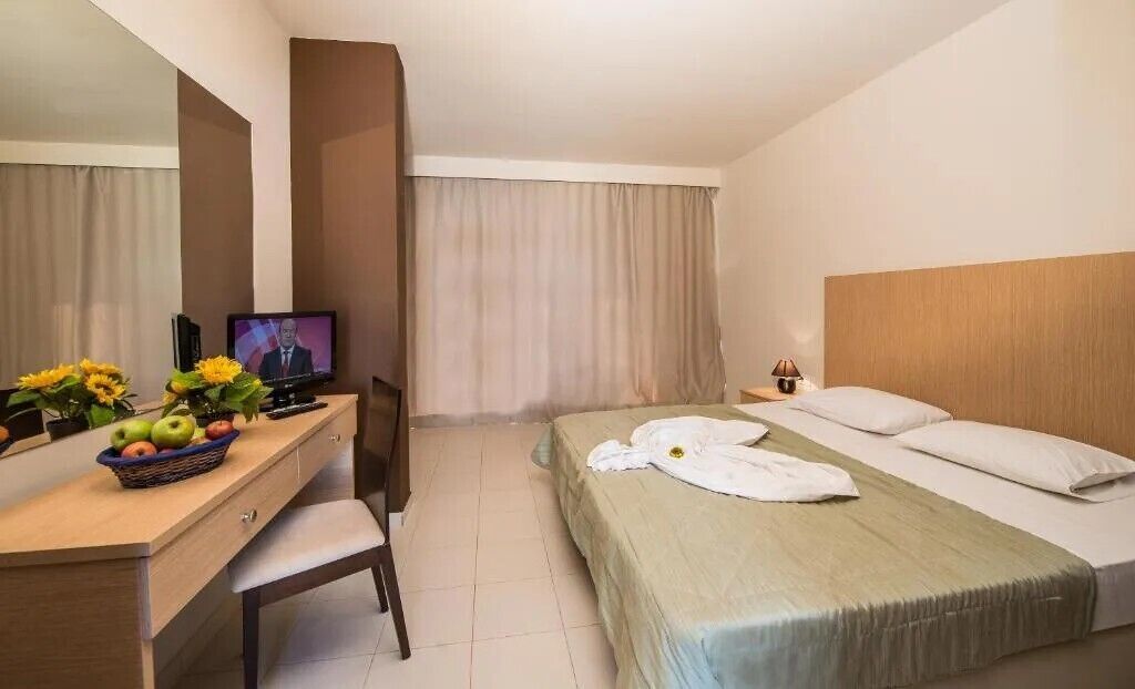 Habitación de hotel con cama, escritorio, computadora, silla y ventana con cortinas.