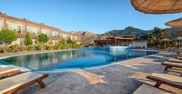 Relax by the pool surrounded by lush trees and a mountain backdrop.