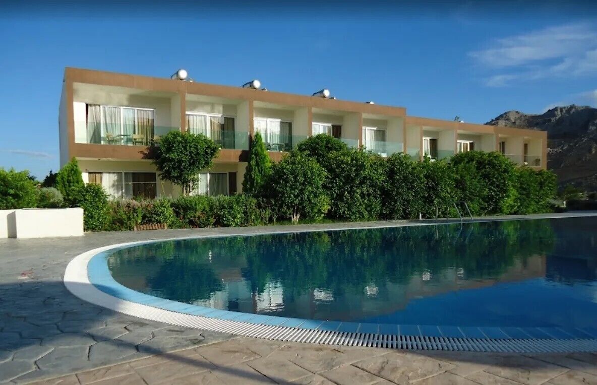 Hotel moderno com piscina, cercado por vegetação exuberante e montanhas ao fundo.