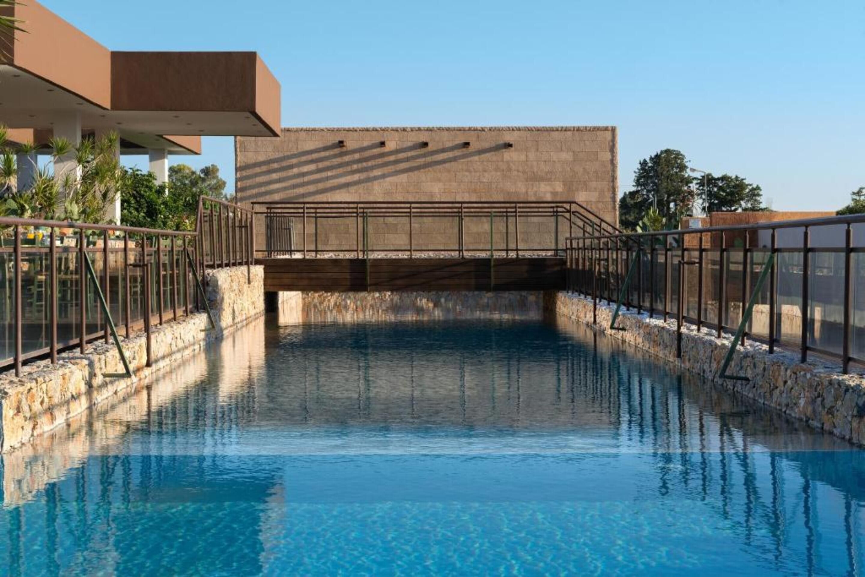 A swimming pool with a stone border, a metal railing, and a building in the background.