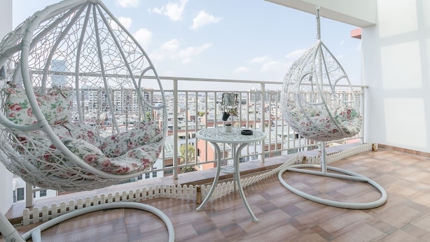 A balcony with two white wicker swing chairs with floral cushions, a small round table, and a white picket fence. - Le Tu Community (Kunming)