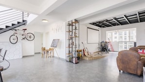 A spacious living area with a staircase, a bookshelf, a painting on easels, and musical instruments. - Le Tu Community (Kunming)
