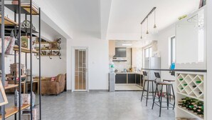 A spacious kitchen with modern appliances, a bar area with stools, and a bookshelf filled with decorative items. - Le Tu Community (Kunming)