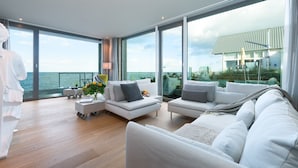 A modern living room with a large window overlooking the sea, furnished with white sofas and a coffee table. - "Heimathafen 2" vacation apartment with sauna, south-facing terrace & roof terrace by the water (Olpenitz)