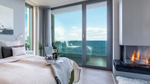 A modern bedroom with a large bed, a fireplace, and a balcony with a view of the sea. - "Heimathafen 2" vacation apartment with sauna, south-facing terrace & roof terrace by the water (Olpenitz)