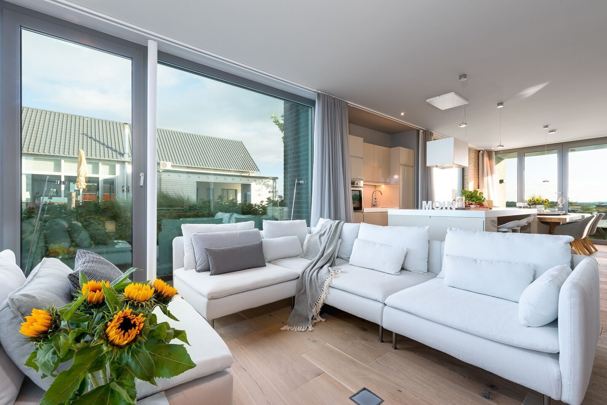 A modern living room with a white sofa, a coffee table, and a large window offering a view of the outside.