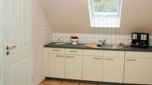 Una piccola cucina con mobili bianchi, un piano di lavoro nero, una finestra sopra il lavello e una porta a sinistra.