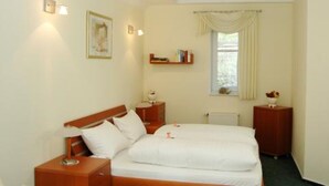 Camera d'albergo con un letto singolo, comodini, una libreria e una finestra con tende.