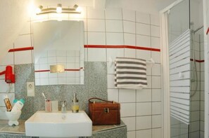 Casa de banho com lavatório branco, espelho, porta-toalhas e uma toalha vermelha.