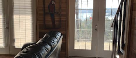 A room with a black leather sofa, wooden walls, a wooden ceiling, and a view through a glass door.