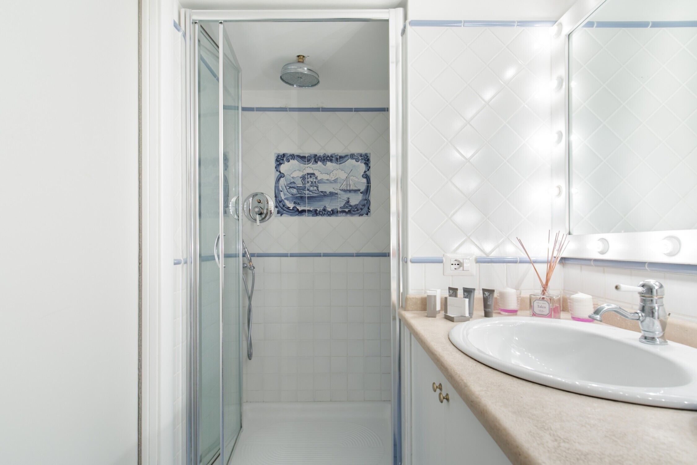 Een badkamer met een douchecabine van glas, een wastafel met spiegel en een decoratieve tegelachtergrond.