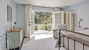 Une chambre à coucher avec un lit, une table de chevet, une commode et une chaise. Il y a une fenêtre avec des rideaux et une vue sur l’extérieur.