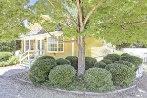 A yellow house with a white fence, surrounded by well-maintained bushes and a gravel driveway. - Private 1300 sq ft Cottage in Historic Yorktown-w/ trolley access (Yorktown)