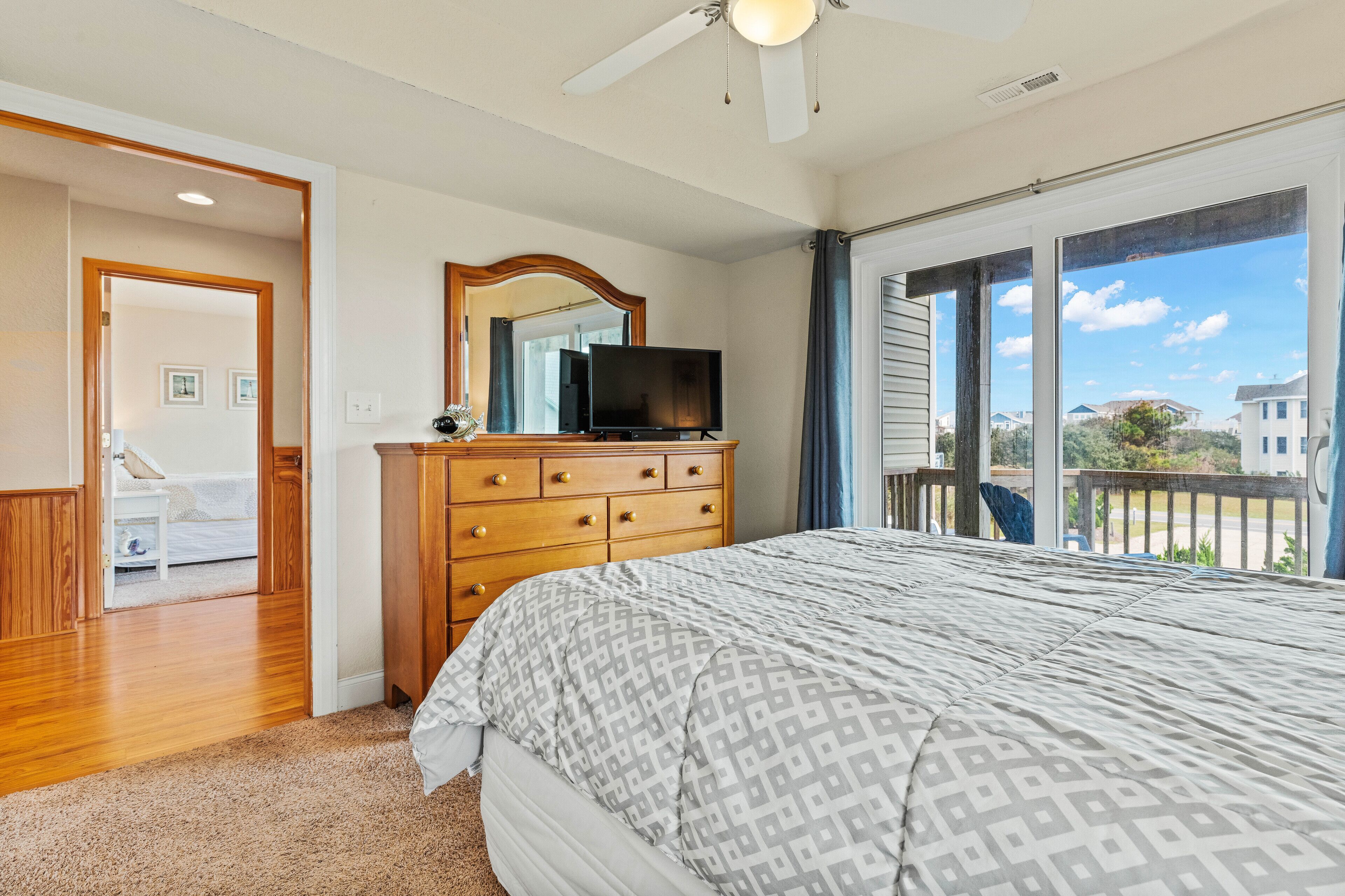 A bedroom with a bed, dresser, television, and a balcony with a view.