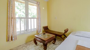 A room with a bed, a wooden table, a chair, and a window with curtains. - Hotel Kayu Manis (Pakem)