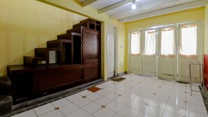 A room with a tiled floor, a wooden staircase, a door with curtains, and a red bench. - Hotel Kayu Manis (Pakem)