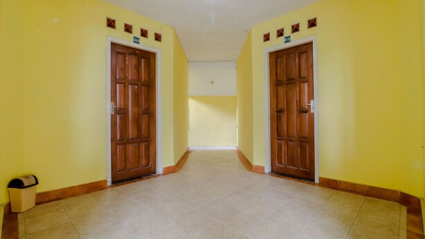A hallway with yellow walls, wooden doors, and tiled flooring. - Hotel Kayu Manis (Pakem)