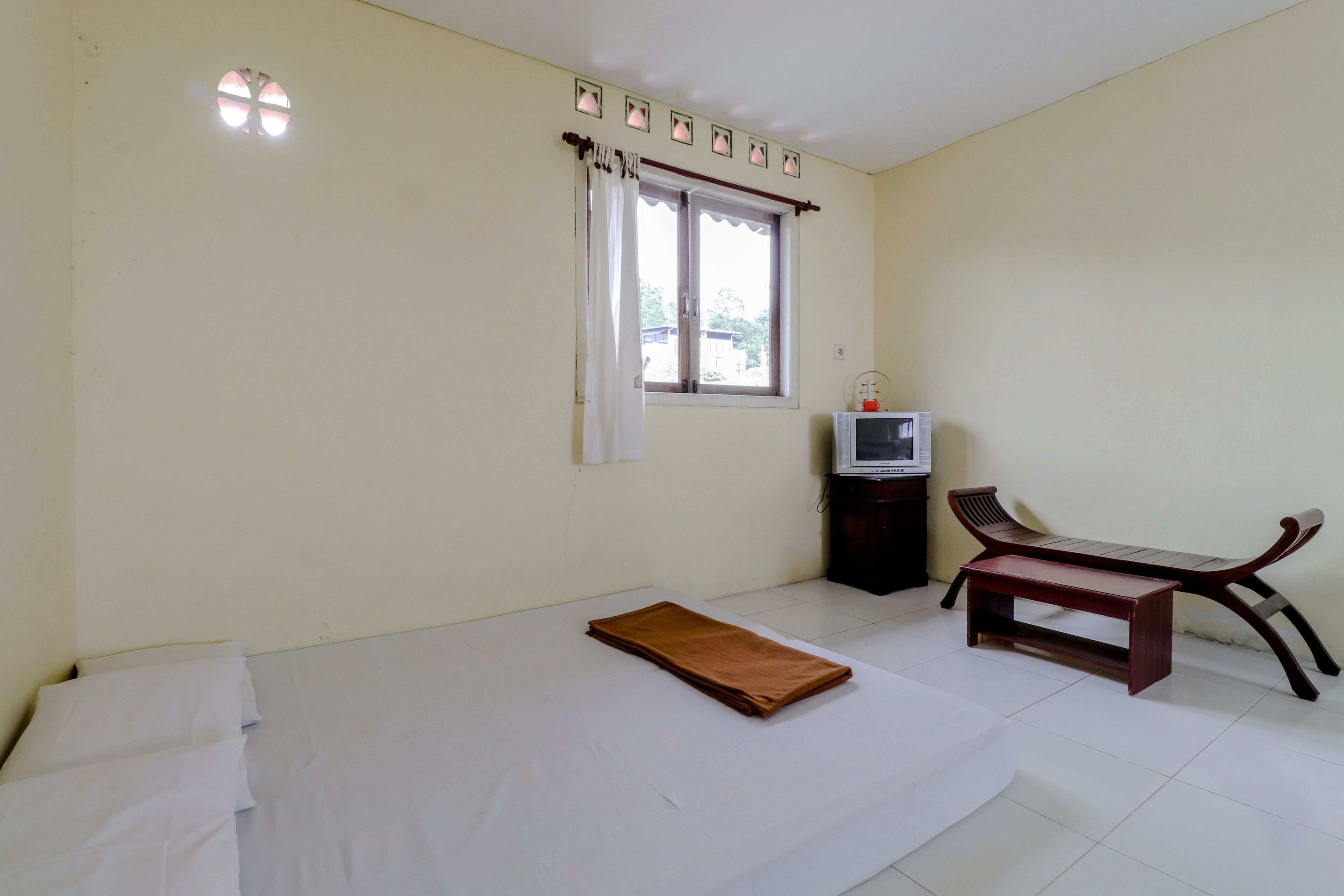A room with a bed, a bench, a TV, and a window with curtains.