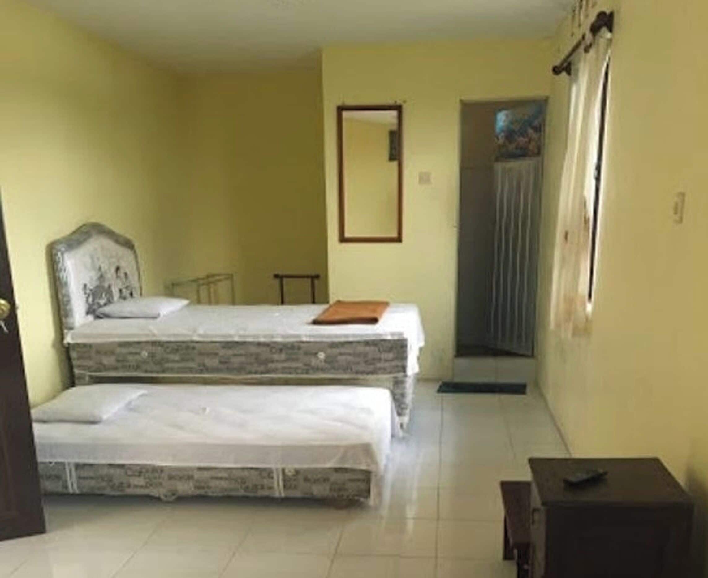 A room with two beds, a small table, and a door leading to another room.