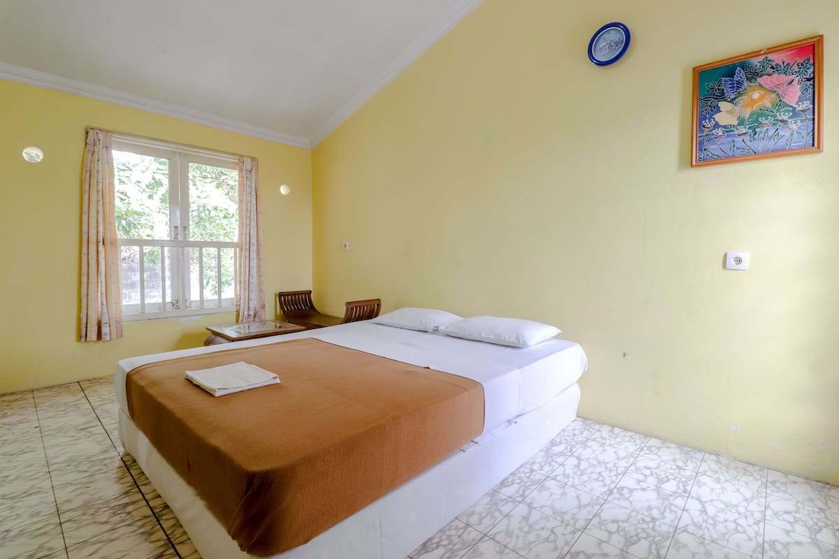 A hotel room with a bed, a window with curtains, a painting on the wall, and a tiled floor.