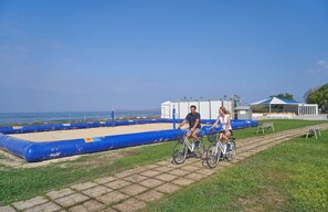 Ein gepflasterter Weg mit zwei Fahrrädern, einer blauen aufblasbaren Barriere und einem weißen Gebäude mit blauem Dach im Hintergrund.