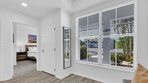 A hallway with a large window, a door, and a bed with a nightstand. - WATERLILY at Greenlinks - Updated Condo with Captivating Views! (Naples)