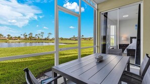 A room with a large window overlooking a grassy area and a body of water, with a dining table and chairs inside. - WATERLILY at Greenlinks - Updated Condo with Captivating Views! (Naples)