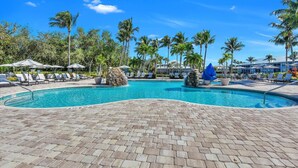 A swimming pool with lounge chairs and umbrellas, surrounded by palm trees. - WATERLILY at Greenlinks - Updated Condo with Captivating Views! (Naples)