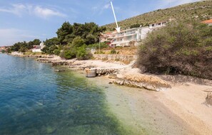 Une zone côtière avec des eaux cristallines, une plage de sable et un bâtiment portant l’inscription « APPARTEMENTS ALENKA ».