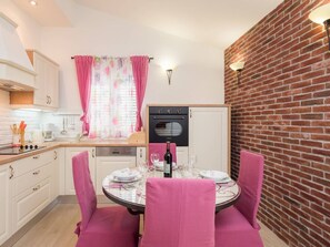 Uma área de refeições com uma mesa redonda, cadeiras cor-de-rosa, uma garrafa de vinho e uma parede de tijolos.