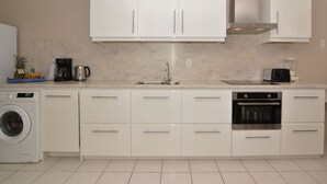 Une cuisine moderne avec des meubles blancs, un four encastré et un lave-linge.