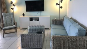 Un salon doté d’un téléviseur à écran plat, de meubles en osier, d’un meuble de rangement blanc et de deux lampadaires.