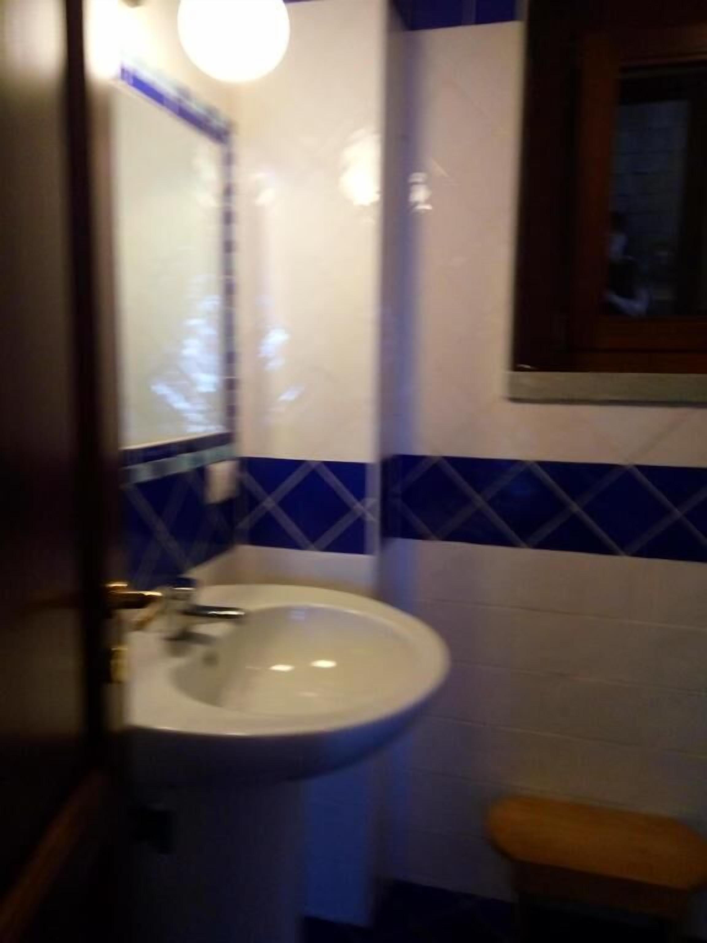 Un baño con un lavamanos blanco, azulejos azul y blanco, y un banco de madera.