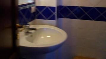 Un baño con un lavamanos blanco, azulejos azul y blanco, y un banco de madera.