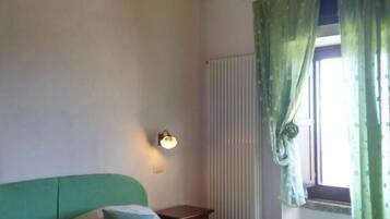 Un dormitorio con una cama verde, una mesita de noche, una lámpara de pared y una ventana con cortinas verdes.