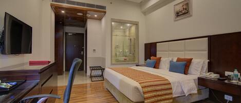 Hotelkamer met een groot bed, een bureau met een flatscreen-tv, een stoel, een douche en een schilderij aan de muur.