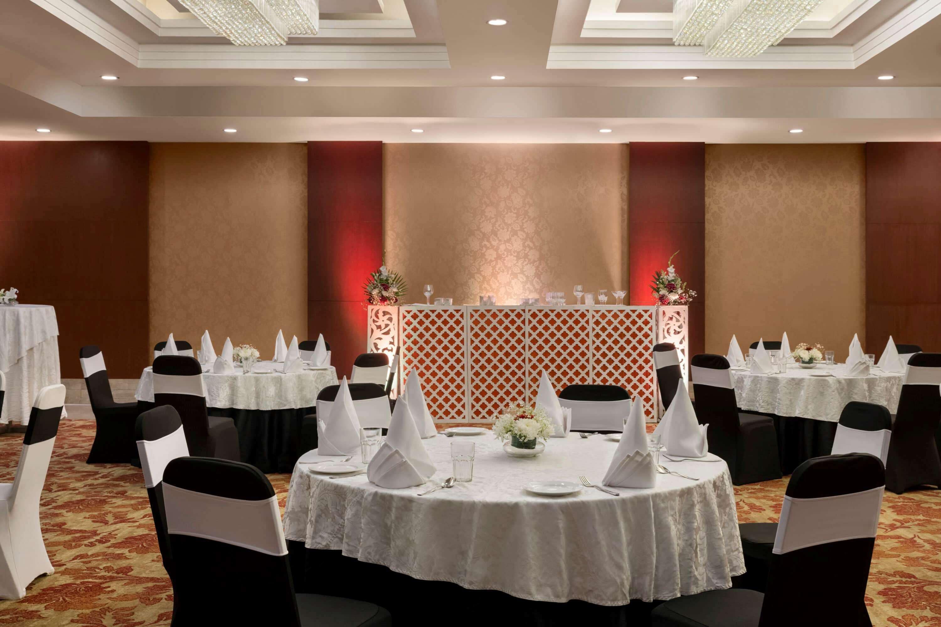 A banquet hall with round tables, black chairs with white sashes, and a decorative backdrop.