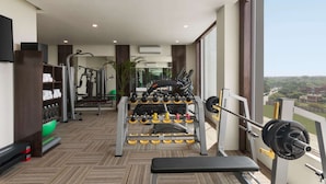 Un gimnasio con varios equipos de ejercicio, una banca y un ventanal que ofrece vistas al exterior.