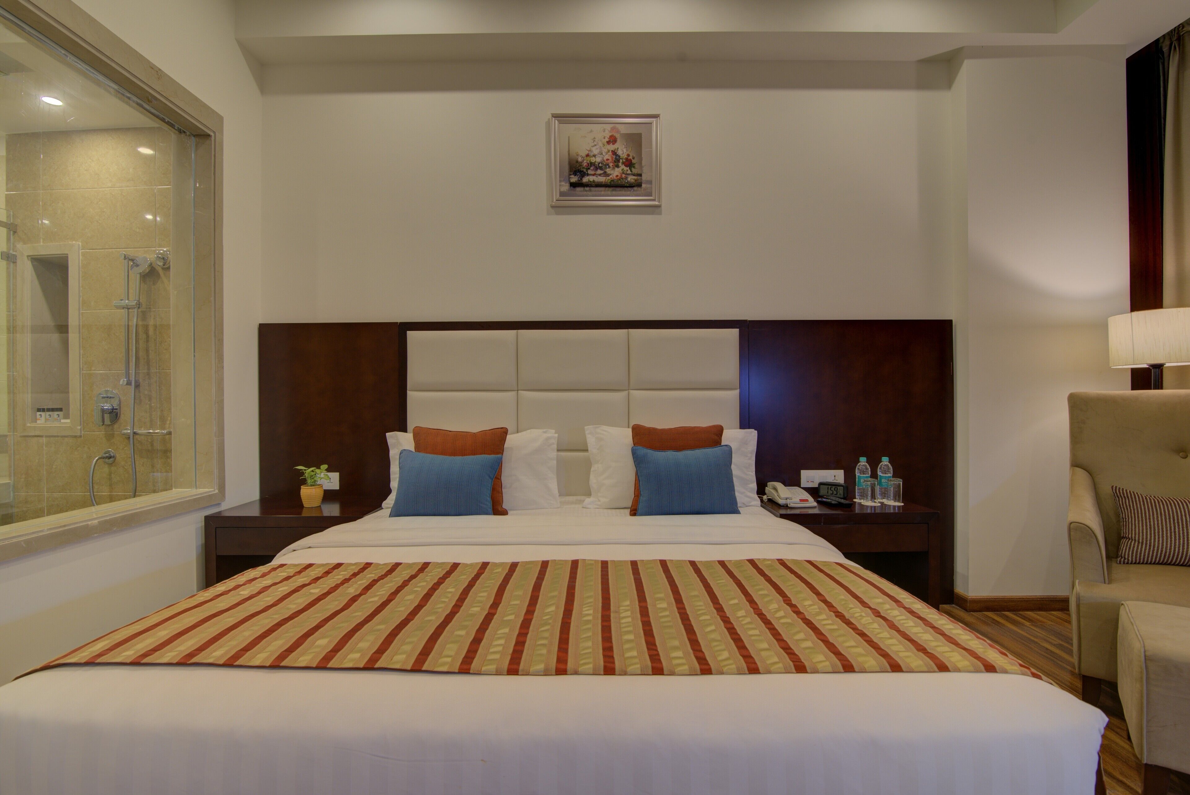 A hotel room with a large bed, a headboard, a bedside table with a lamp, a chair, and a shower area.