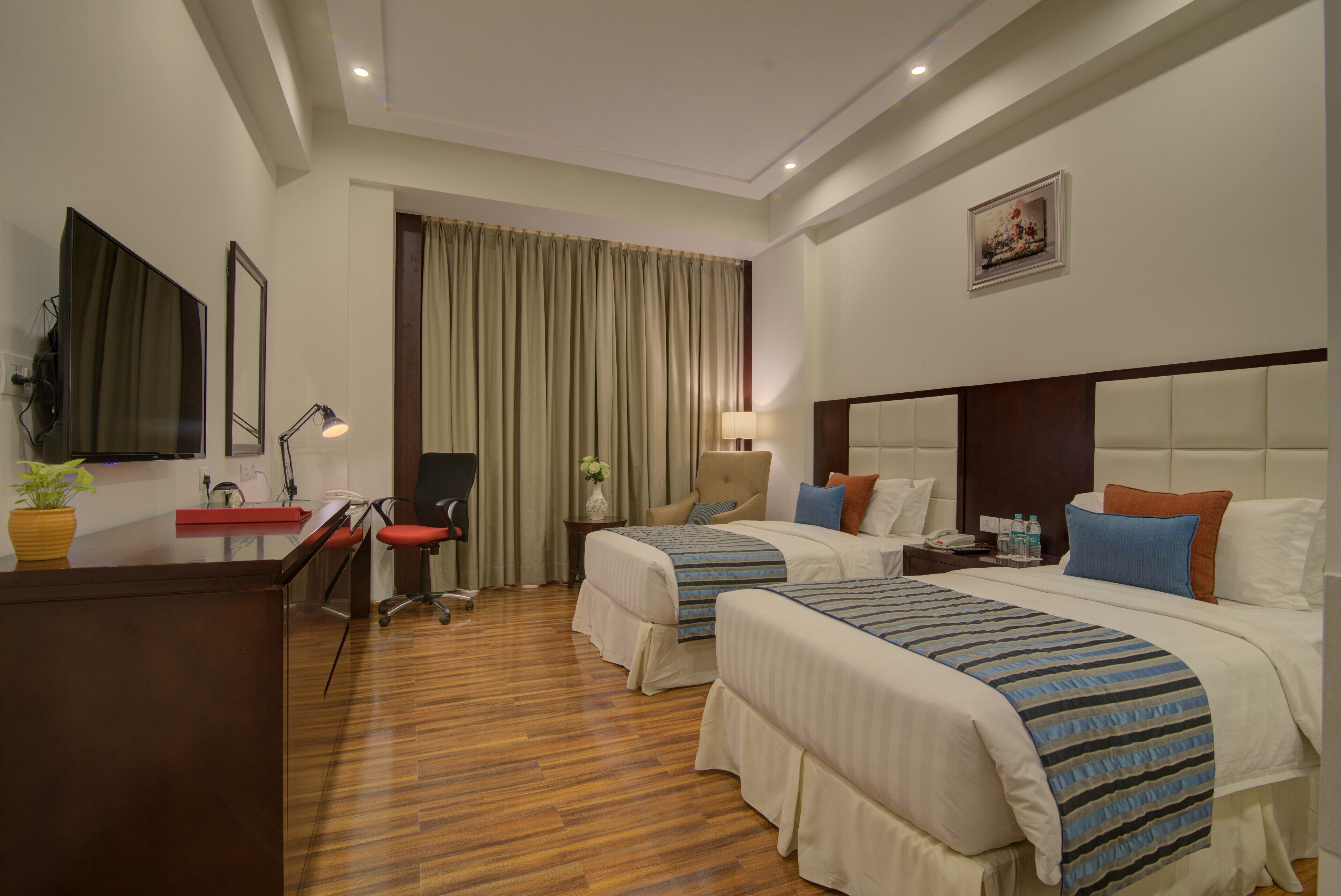 A hotel room with two beds, a desk, a chair, a lamp, and a mirror.
