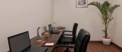 A conference room with a wooden table, black chairs, a laptop, a potted plant, and a framed picture on the wall.
