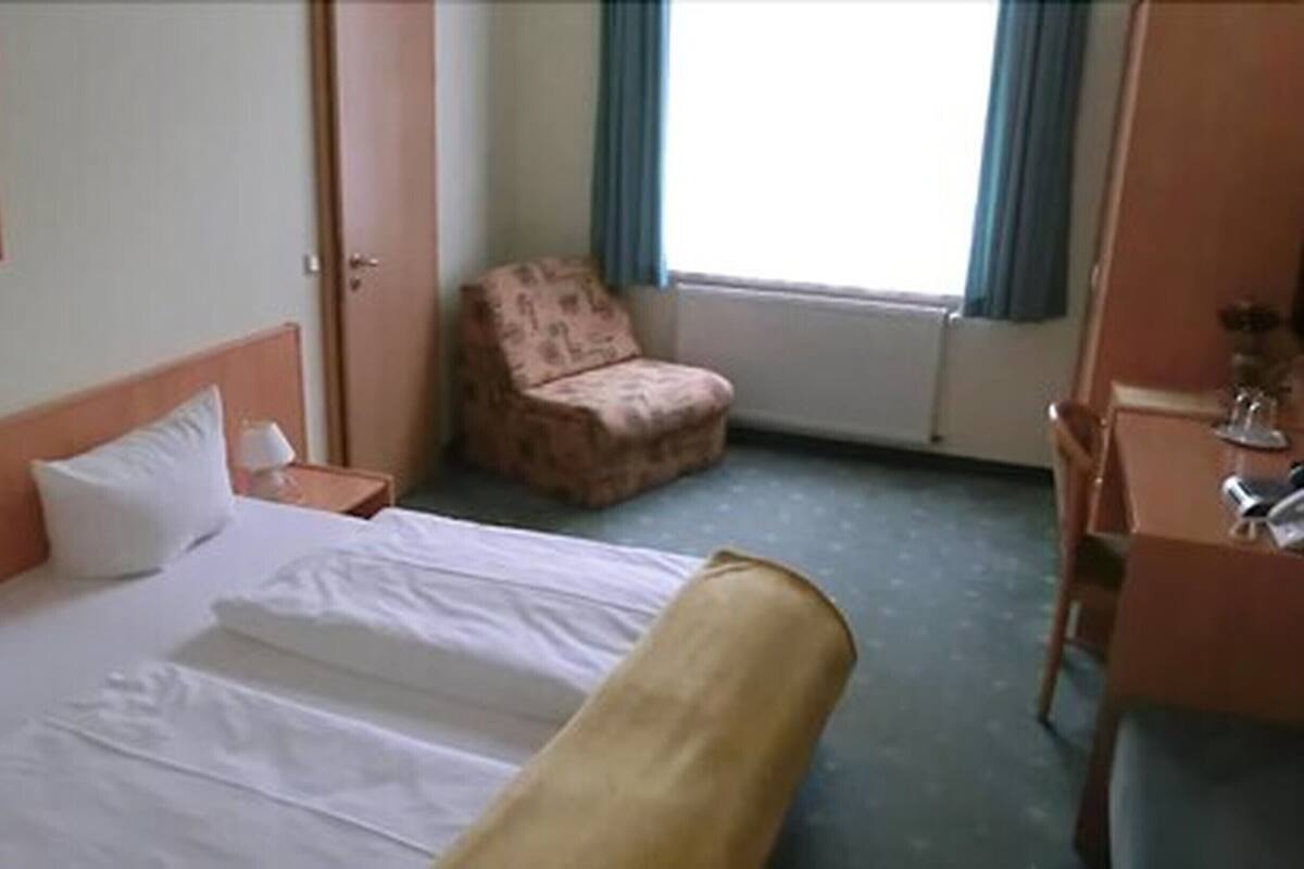 A hotel room with a bed, a chair, a desk, and a window with curtains.