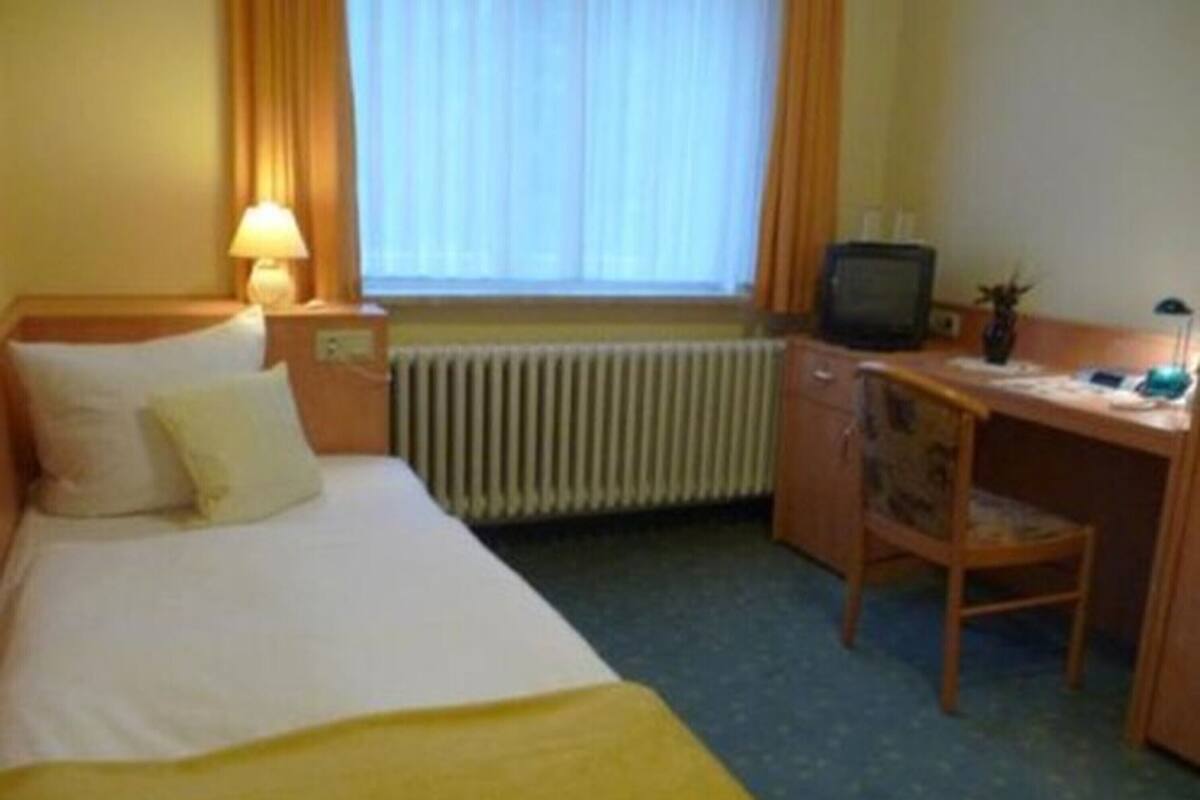 A hotel room with a bed, a desk, a chair, a television, and a window with curtains.