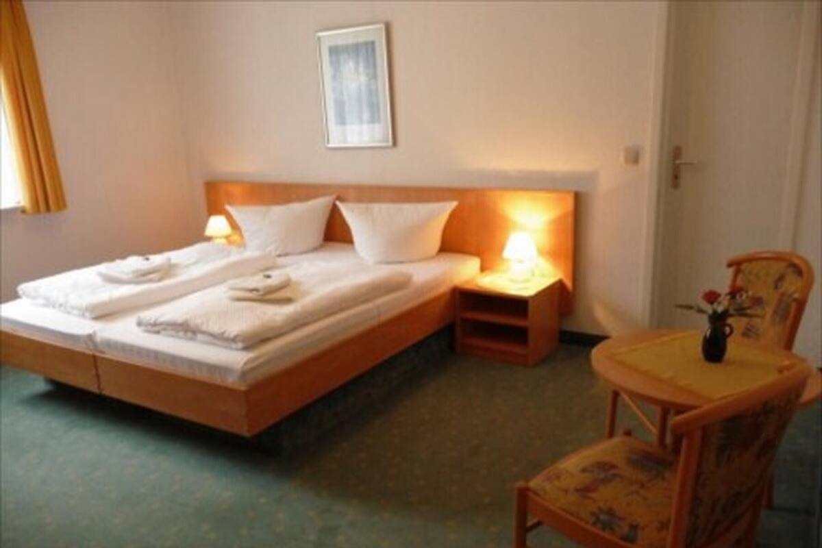 A single bed with a wooden headboard, two bedside tables, a chair, and a small table with a vase.