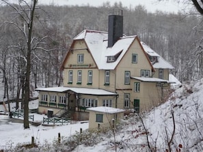 A large, multi-story house with a steep roof, surrounded by snow-covered trees and a hill. - Hotel am Schlosspark (Wernigerode)
